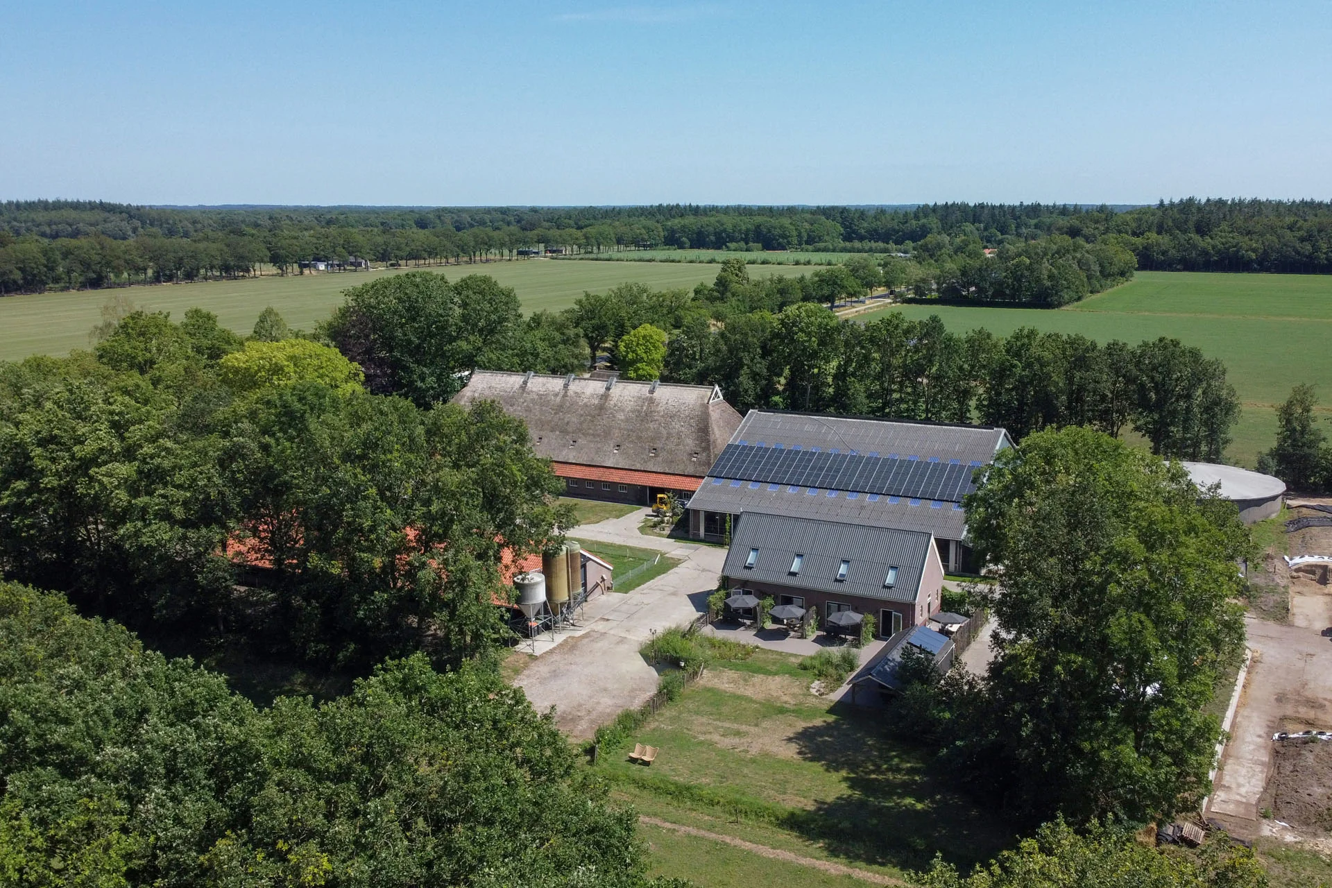 Luchtfoto van de Hoeve met bijgebouwen, bomen en weilanden.